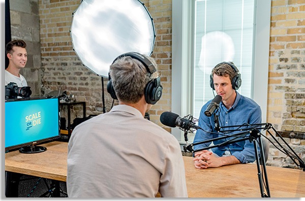 foto de dois homens conversando com headsets e microfone, como se estivessem a gravar podcasts